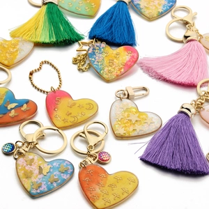 Close-up of heart resin keychains with colorful tassels, glitter, and gold butterfly charms