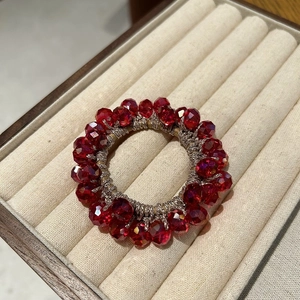 Detailed view of red crystal beads on a silver woven hair tie displayed on velvet