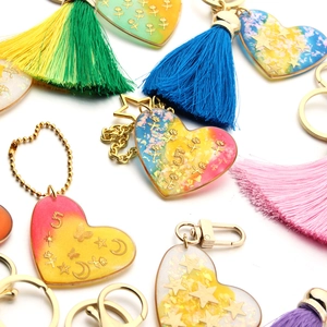 Close-up of colorful resin heart keychains with glitter, gold charms and large tassels