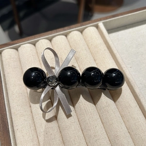 Détail d'une pince à cheveux avec quatre perles noires et un nœud en ruban argenté et cristal