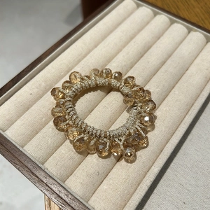 Close-up of champagne crystal bead hair tie displayed on a beige velvet jewelry box