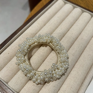 Close-up of white woven pearls elastic hair tie on a beige velvet jewelry tray