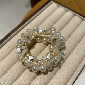 Close-up of pearl hair tie with camellia floral accents on beige velvet tray