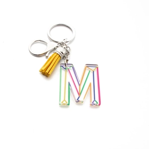 Detail of acrylic letter M keychain with yellow tassel and silver metal clasp