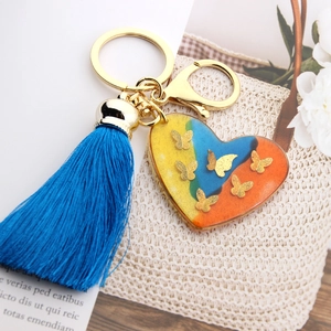 Detail of colorful resin heart keychain with golden butterflies and blue silk tassel