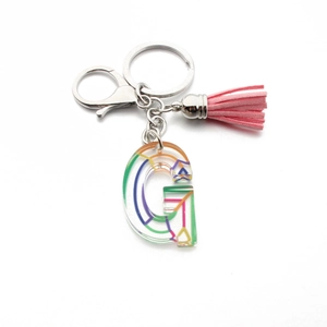 Macro shot of clear acrylic letter G keychain with pink tassel and silver metal clasp