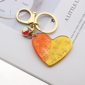 Close-up of heart-shaped resin keychain with golden umbrella pattern and purple charm