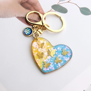 Detail of heart resin keychain with gold butterflies held in hand for scale