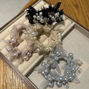 Detail view of pearl mesh hair ties in black, champagne and light blue in a wooden box