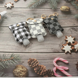 Portable buffalo plaid hand sanitizer bottle holders with gold keychains on festive wood background