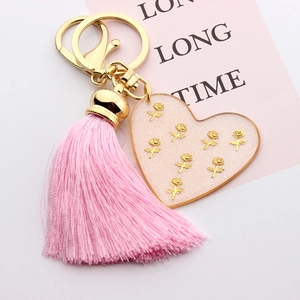 Detailed close-up of pink heart resin keychain with gold roses and tassel ornament