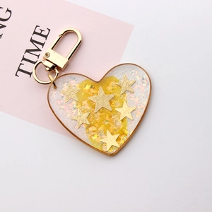 Detail of heart-shaped resin keychain with golden stars and glitter on a pink background