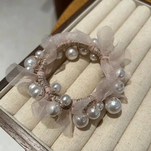 Close-up of champagne pearl and organza scrunchie on a beige jewelry display tray