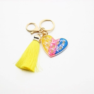 Close-up of resin heart keychain with golden rose sequins and bright yellow silk tassel