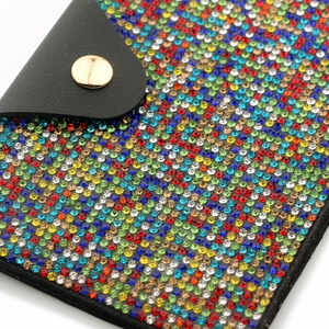 Close-up of colorful rhinestone coin purse with black leather flap and golden button