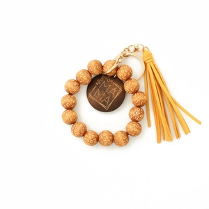 Détail de porte-clés en perles de bois léopard avec pompon jaune et pendentif gravé MAMA