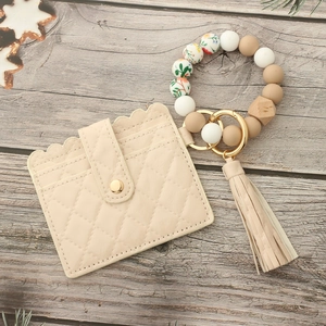Detailed view of beige quilted card holder with beaded silicone wristlet and tassel