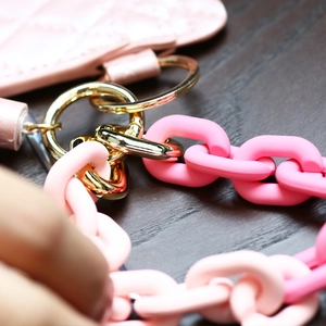 Pink cannage quilted leather wallet with gold ring and acrylic chain on wood background