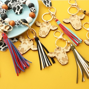 Detail of cow-themed wooden keychain with tassel and beaded bracelet featuring Mama text