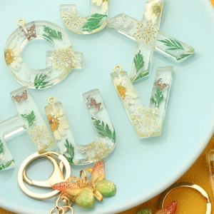 Handmade resin alphabet keychain with dried flowers, butterflies, and gold foil accents