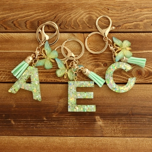 Green resin letter keychain with golden butterfly pendant and tassel on wood background