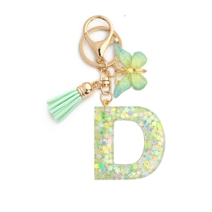 Detailed macro view of resin letter D keychain with green butterfly and silk tassel charm