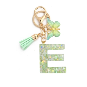 Macro detail of green resin letter E keychain with sequins, butterfly and tassel
