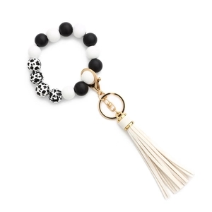 Détail de perles en silicone motif vache et pompon blanc cassé sur le bracelet porte-clés