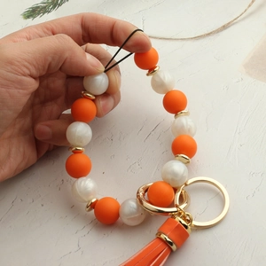 Detail of beaded keychain bracelet featuring orange silicone beads and elegant tassel