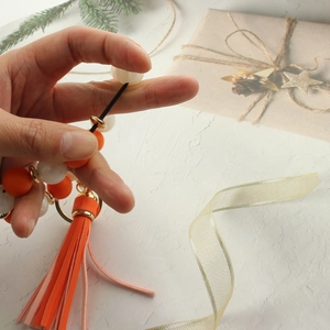 Detail showing the elastic stretch of the orange and white beaded bracelet keychain