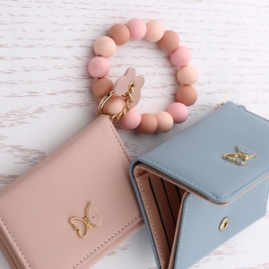 Pink and blue leather butterfly wallets with silicone beaded bracelet and keychain on wood