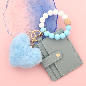Détail du porte-cartes en cuir gris avec pompon coeur et bracelet porte-clés en perles silicone