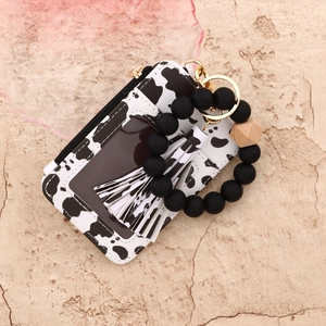 Detail of cow print leather wallet with black silicone beaded bracelet and tassel charm