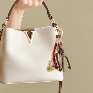Detail von gewebten Lederquasten mit goldenem Sonnenblumen-Anhänger an einer Handtasche