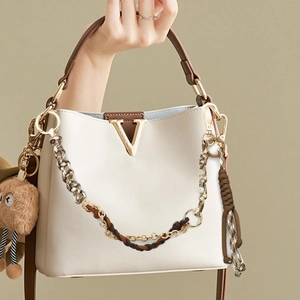 Detail van crème bucket bag met bruine rand, goud V-logo en pluche beer accessoire