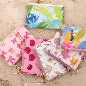 Detail view of mini printed wallets with top zippers and gold metal keychains on stone surface