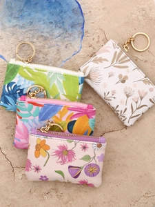 Floral printed mini wallets with gold zippers and keychains set on stone background