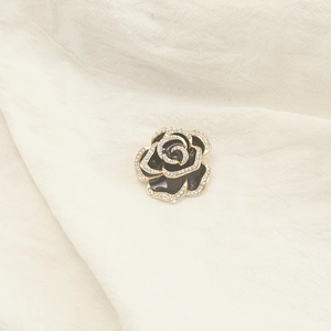 Detailed close-up of black enamel rose brooch with golden edges and sparkling rhinestones