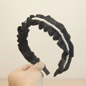 Elegant black velvet pleated headband featuring white faux pearls on a beige background