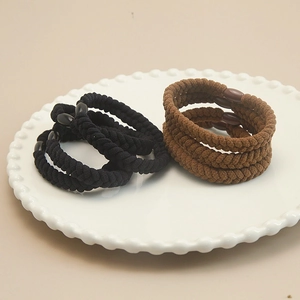 Elastic braided hair ties in black and brown colors on a white ceramic tray