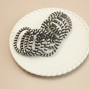 Detail of hand-woven black and white spiral hair ties with beads on a ceramic plate