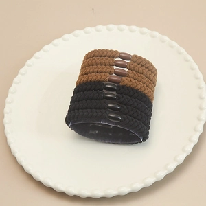 Detail view of woven high-elastic hair ties in black and coffee brown on a ceramic tray