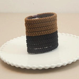 8-piece set of thick elastic braided hair ties in brown and black on a ceramic plate