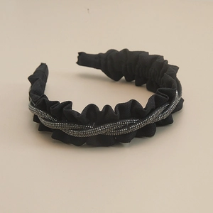 Elegant black pleated headband with spiral glitter accents on a clean beige surface