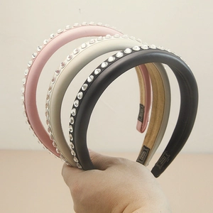 Close-up of three padded leather headbands with rhinestones in pink, grey, and black colors