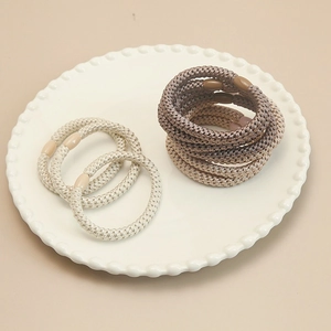 Close-up of high-elasticity braided hair ties in neutral earth tones on a white ceramic plate