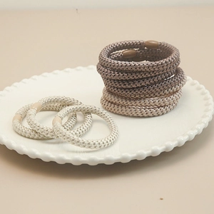 Handmade elastic braided hair ties set in earthy tones on a white ceramic tray