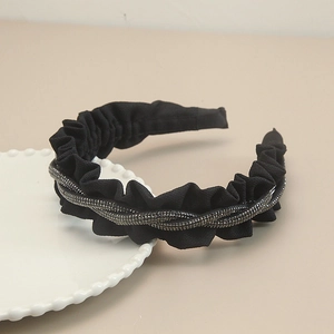 Detail of a black pleated fabric headband with double-row bead embellishments on a ceramic plate