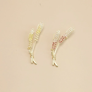 Close-up of golden wheat brooch with yellow and pink cubic zirconia on beige background