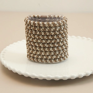 Close-up of brown and beige hand-woven elastic hair ties on a white decorative plate